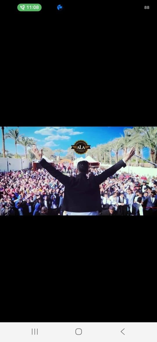 Dr. Ahmed Latif with open arms on stage with fire sparks effects in a large crowded auditorium