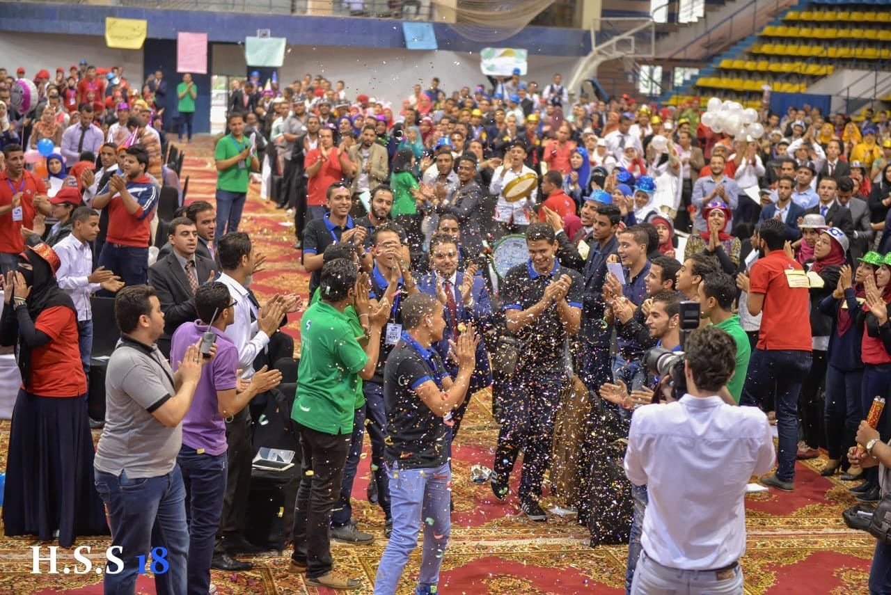 Dr. Ahmed Latif addressing a huge outdoor crowd with arms raised during a public event