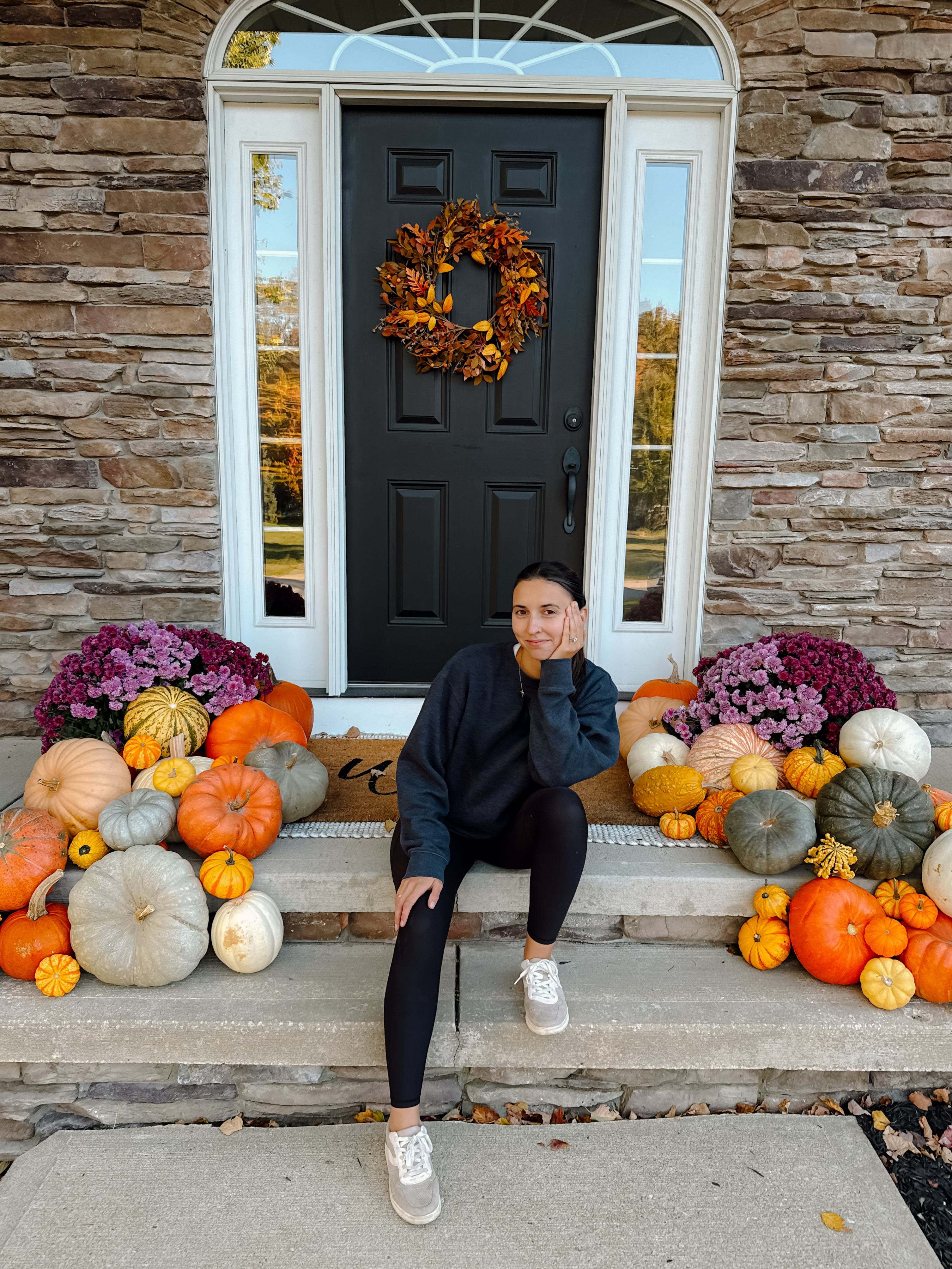 Front door styled with a fall wreath, mums, and layered pumpkins
