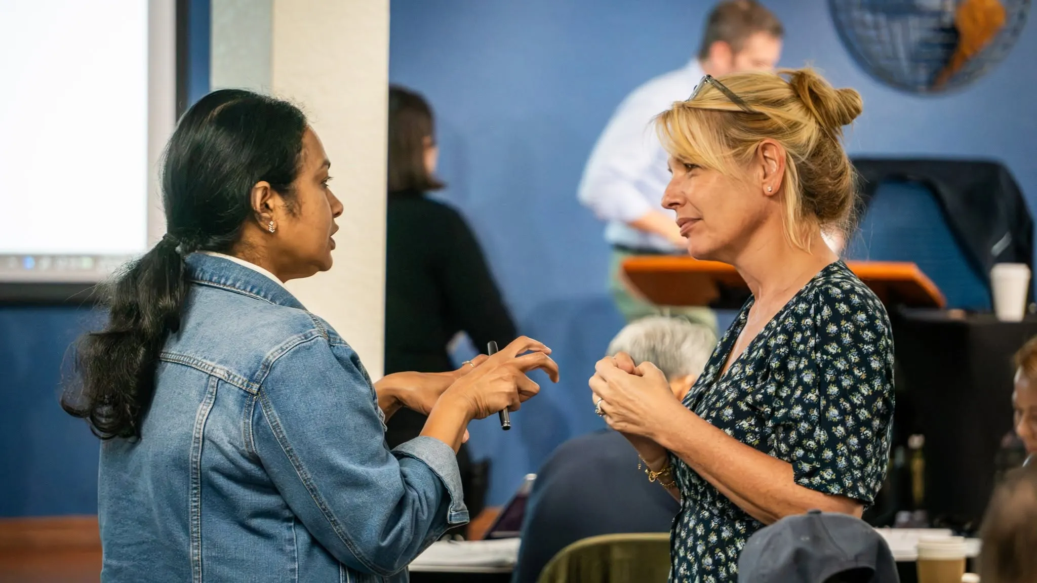 Two attendees talking during a seminar break, one gesturing with a pen