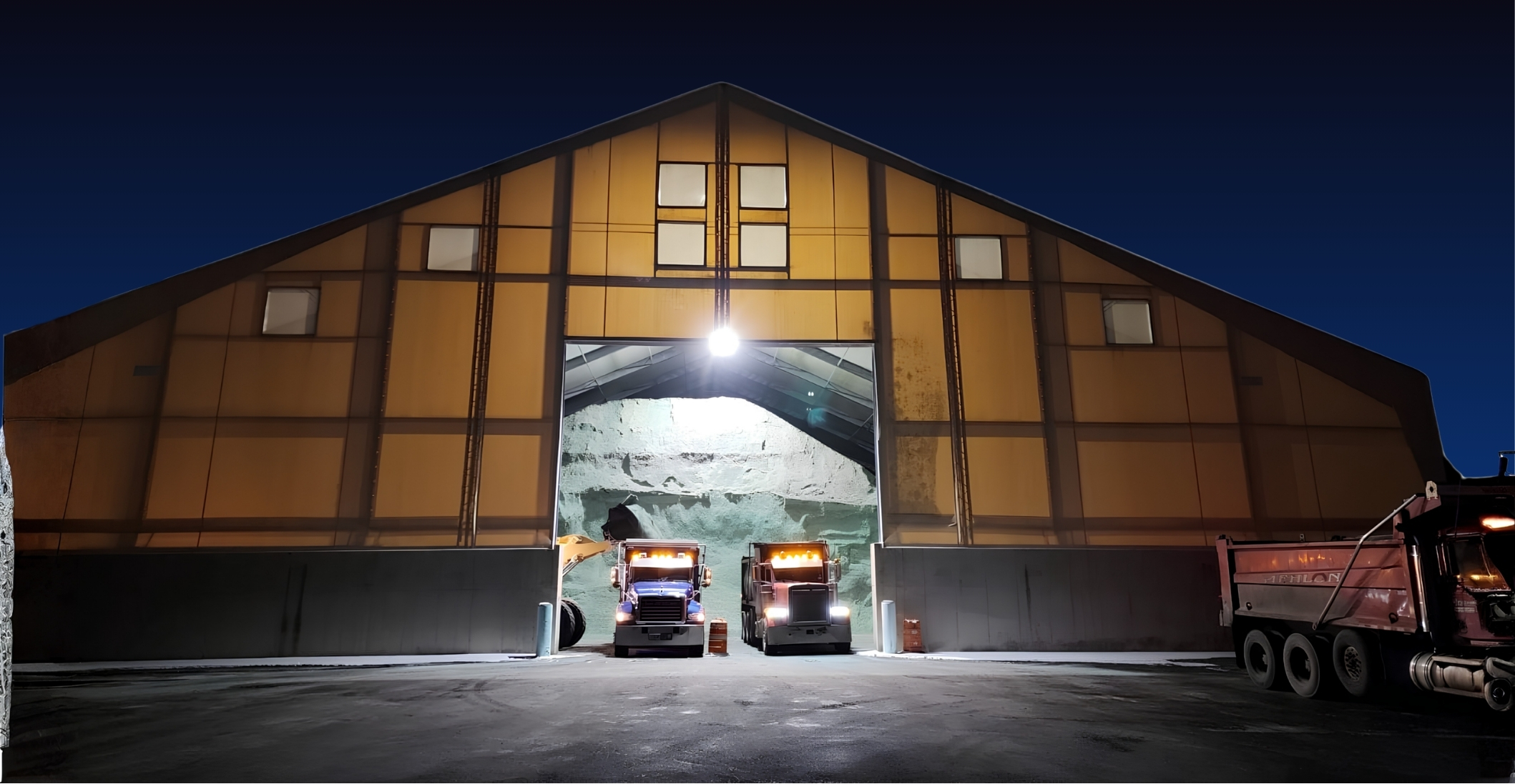Aden salt storage building at night, two trucks loading salt at the open door