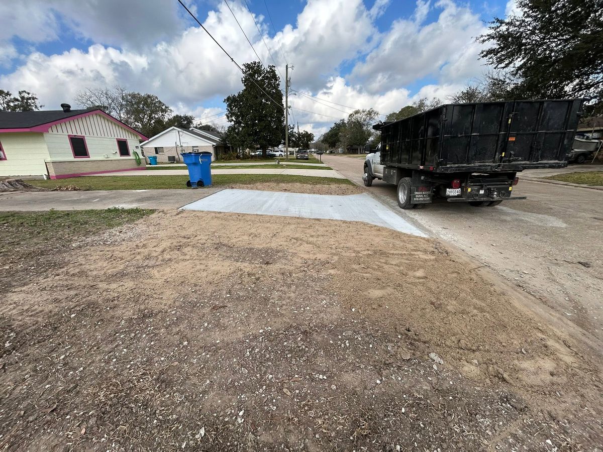 Graded job site with a dump truck beside a newly poured concrete apron