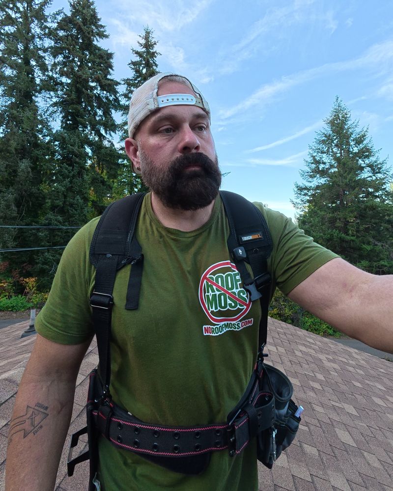 Shane, owner of Sedona Home Services, on a roof in front of tall fir trees