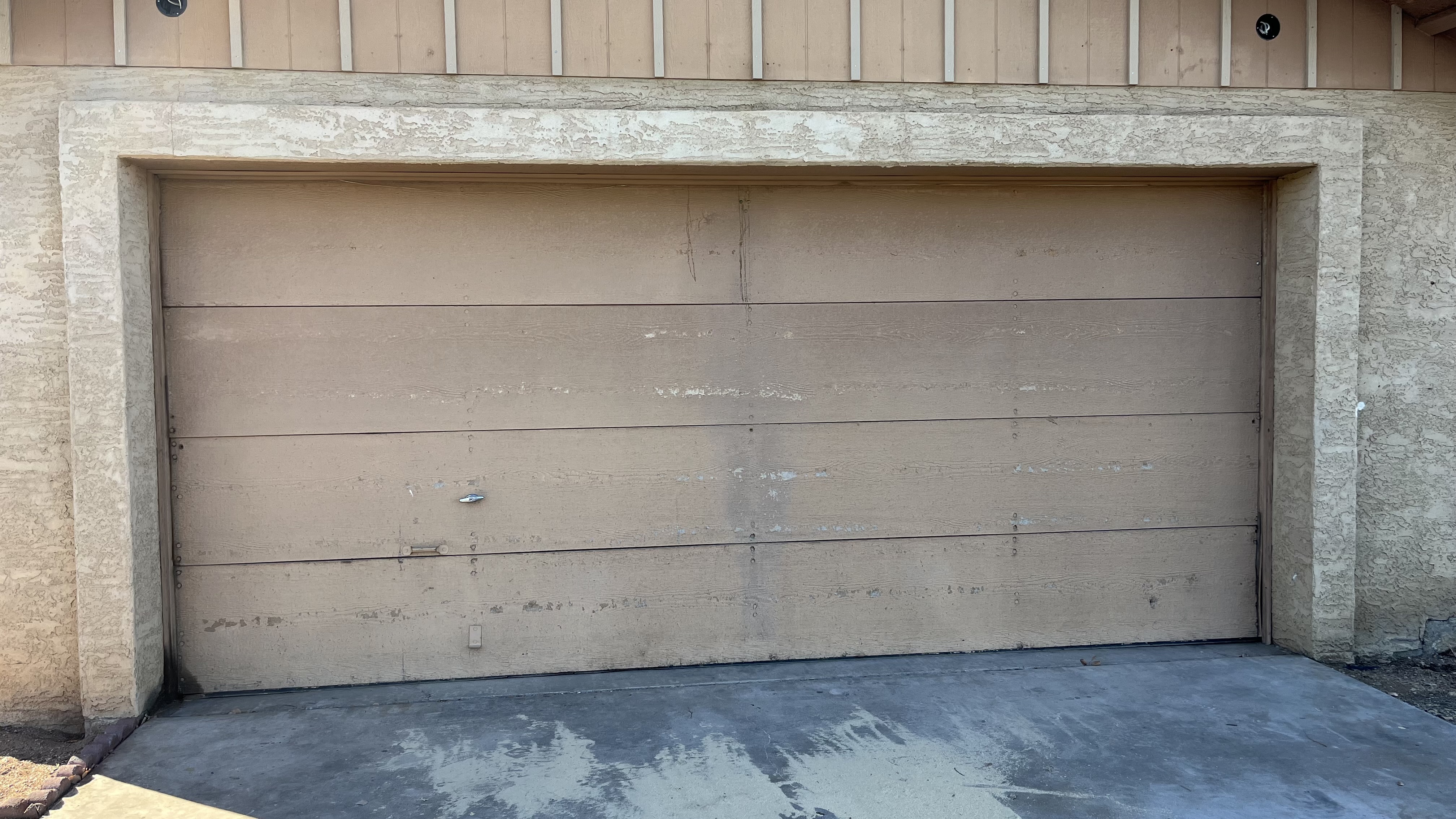 Old, sun-bleached and dented garage door on a Mesa Arizona stucco home before replacement