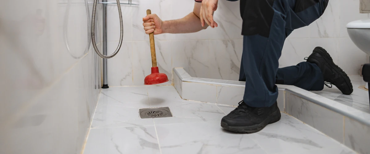 Plumber using a plunger to unclog a shower floor drain