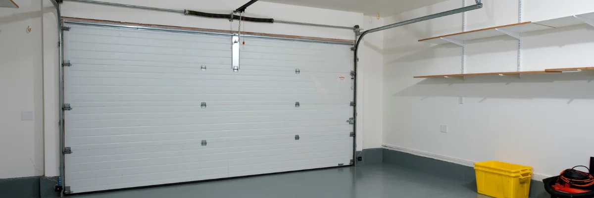 Clean residential garage interior with white garage door and wall shelves.