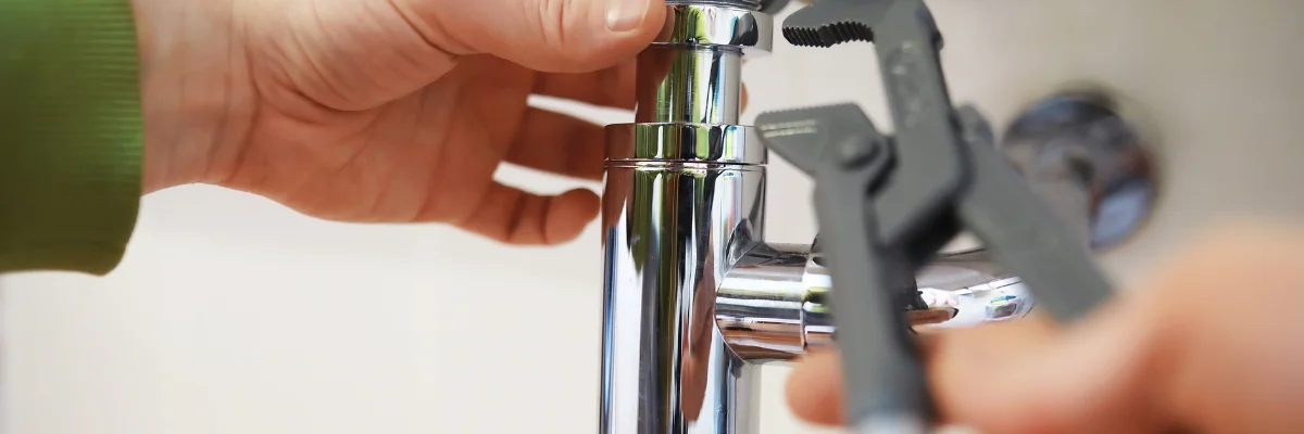 Plumber repairing bathroom sink drain pipe underneath sink.