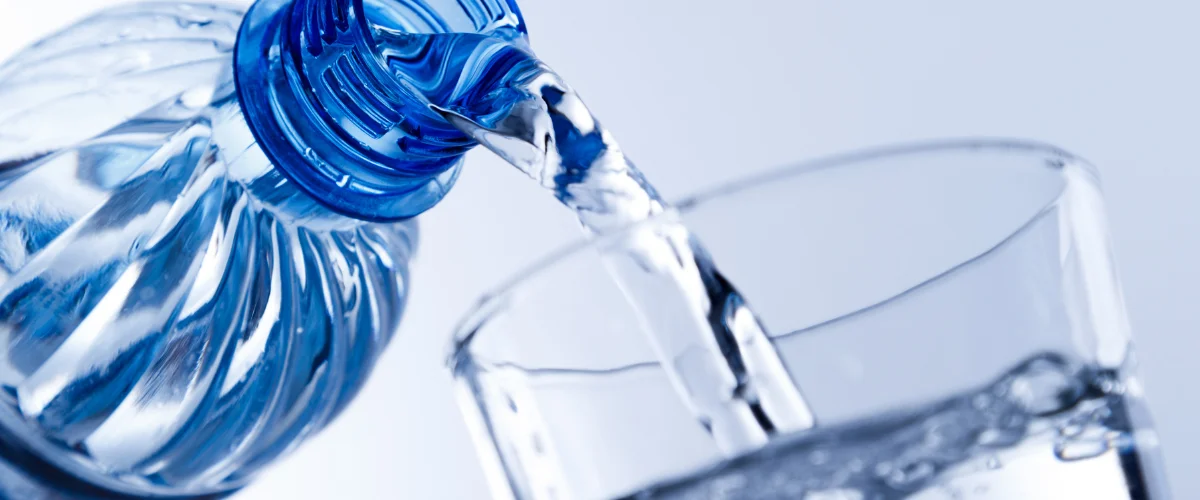 A close-up view of two white and black water filter cartridges next to a clear glass of water.