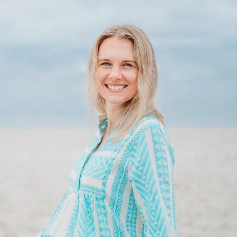 Nikki Gianni smiling on the beach, wearing a turquoise patterned blouse, representing her coaching program focused on developing new school leaders and productivity strategies.