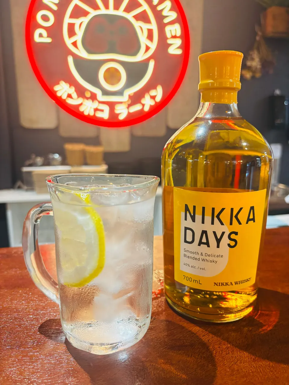 Nikka Days whisky bottle beside a Nikka highball with lemon, under the Pompoko neon sign