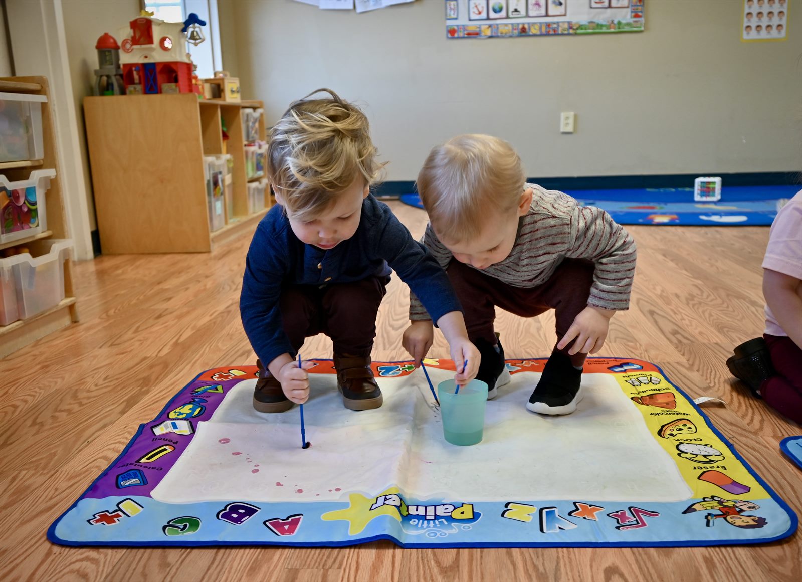 Two toddlers painting together at an activity mat in our classroom