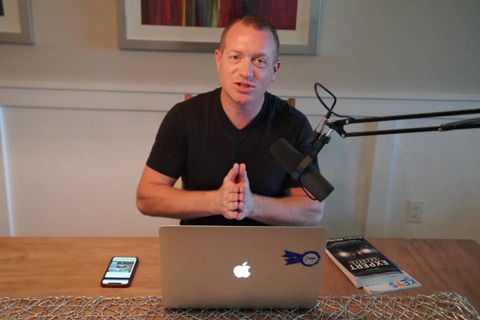 Gene Slade records the Blackbelt Sales Podcast at a desk with a studio microphone and laptop