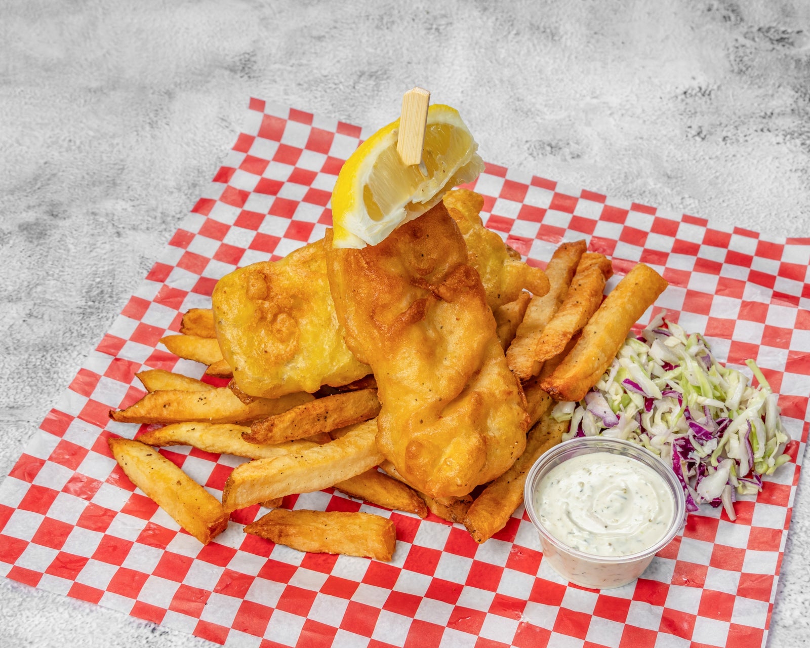 Two pieces of battered halibut with hand-cut chips, lemon wedges, and tartar sauce