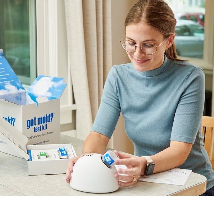 Woman holding a GOT MOLD? air sampling pump next to an open test kit box