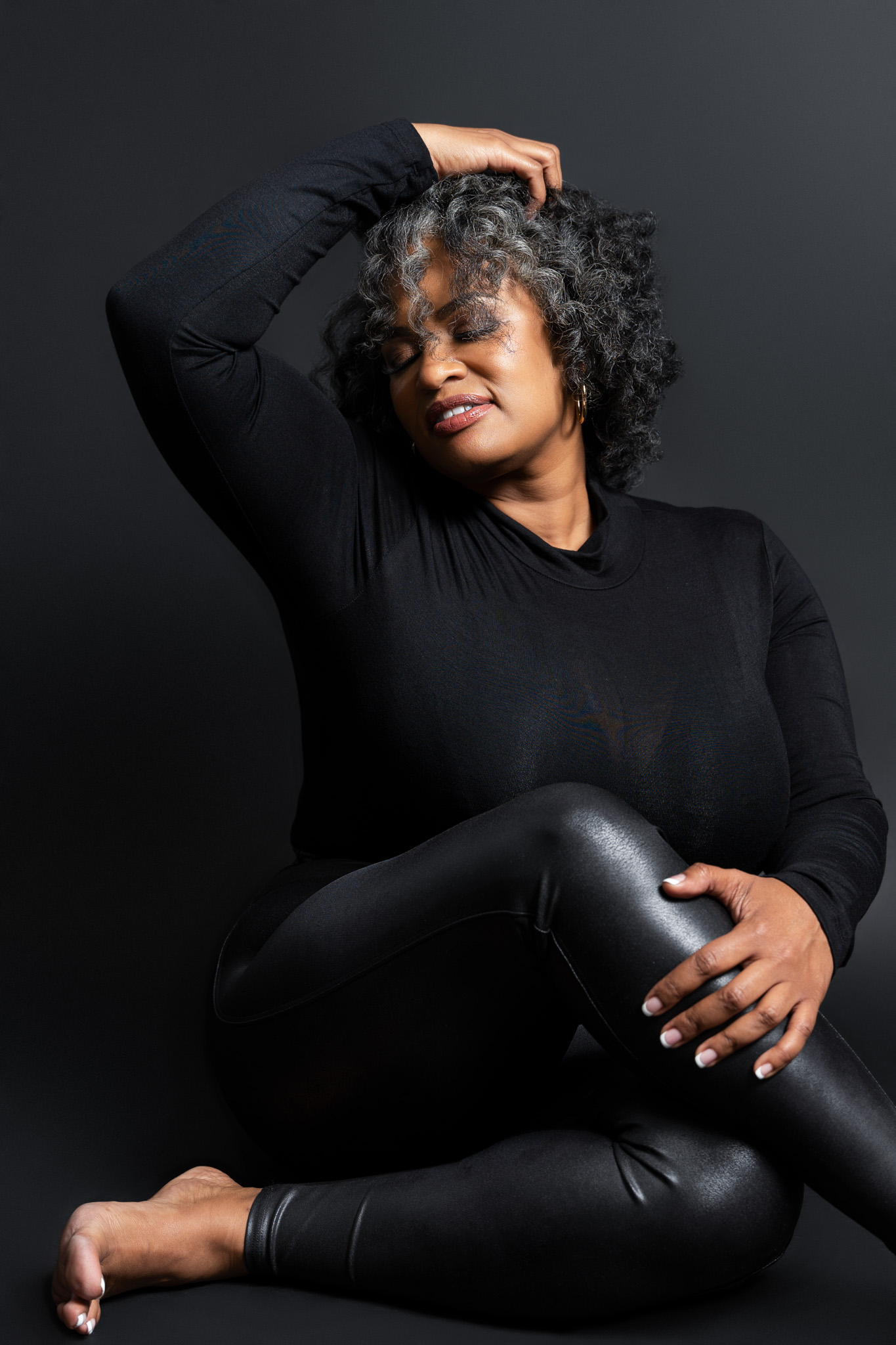 Empowering studio portrait of a woman with natural curls posing in an all-black outfit against a dark backdrop with soft dramatic lighting | Jessica Korff Studios Tucson, AZ Empowering studio portrait of a woman with natural curls posing in an all-black outfit against a dark backdrop with soft dramatic lighting | Jessica Korff Studios Tucson, AZ