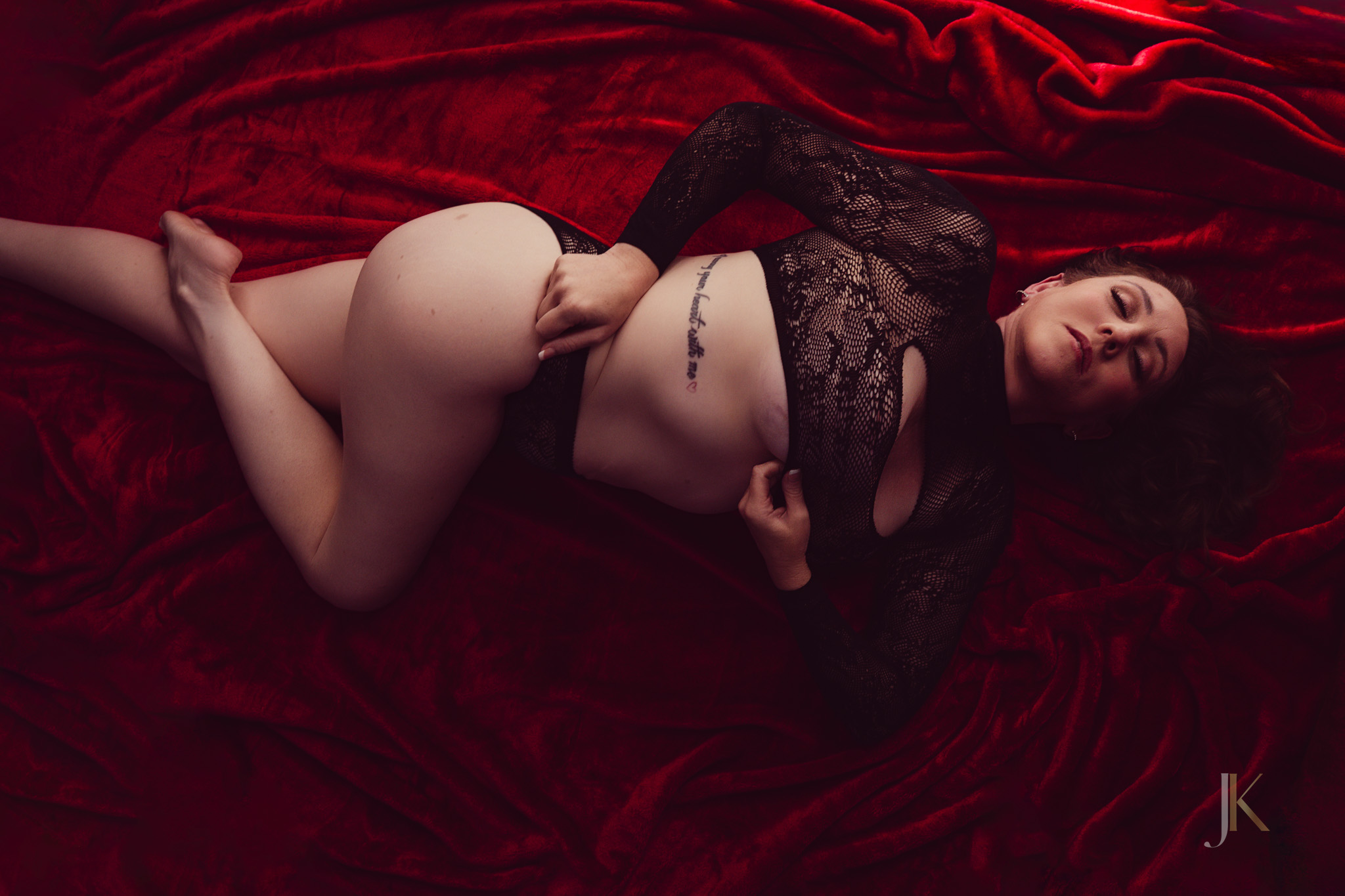 Moody boudoir portrait of a tattooed woman posing on deep red velvet fabric in black lace lingerie with dramatic lighting and sensual styling | Jessica Korff Studios Tucson, AZ Moody boudoir portrait of a tattooed woman posing on deep red velvet fabric in black lace lingerie with dramatic lighting and sensual styling | Jessica Korff Studios Tucson, AZ