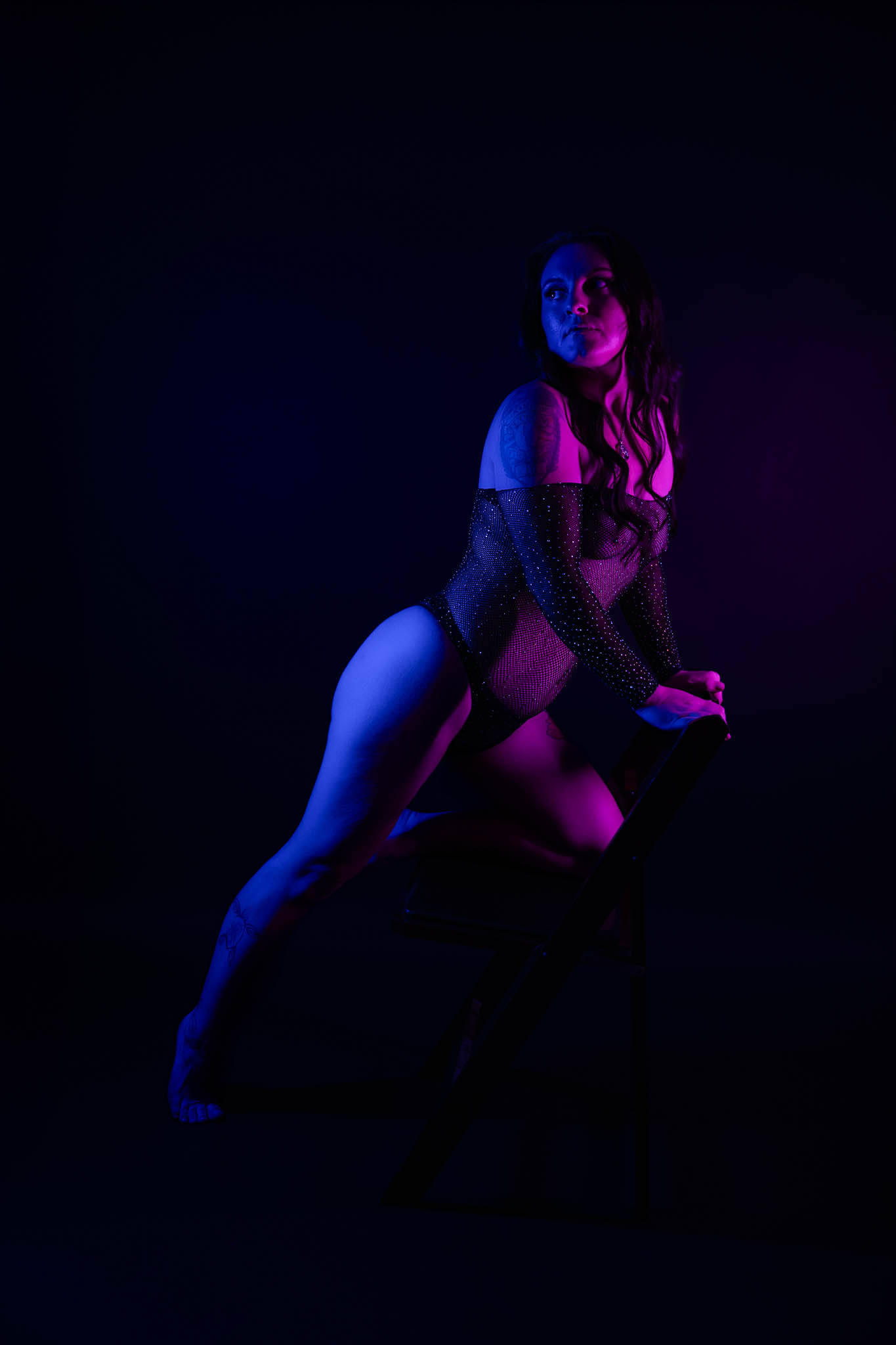 Dramatic neon boudoir portrait of a woman posing in sheer black lingerie with purple and blue lighting against a dark studio background | Jessica Korff Studios Tucson, AZ Dramatic neon boudoir portrait of a woman posing in sheer black lingerie with purple and blue lighting against a dark studio background | Jessica Korff Studios Tucson, AZ