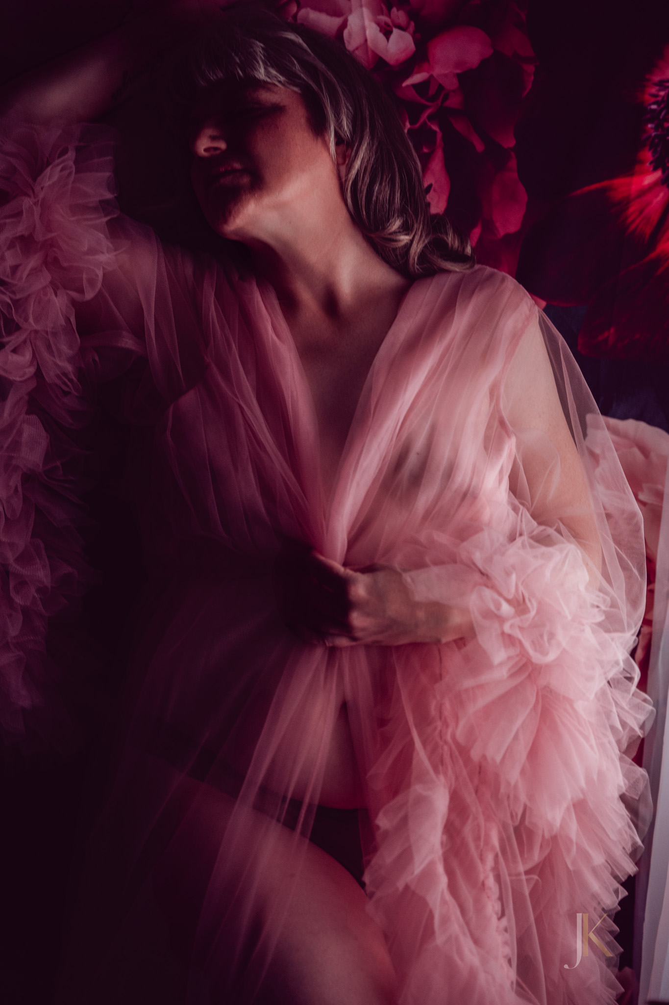 Woman in a flowing blush pink robe posing against a dark floral backdrop, softly lit near a window with a palm leaf in the foreground, creating a moody, romantic atmosphere | Jessica Korff Studios in Tucson, Arizona