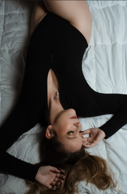 Woman lying on a white bed in a black long-sleeve bodysuit, softly posed with relaxed hands and a calm, confident expression | Jessica Korff Studios in Tucson, Arizona