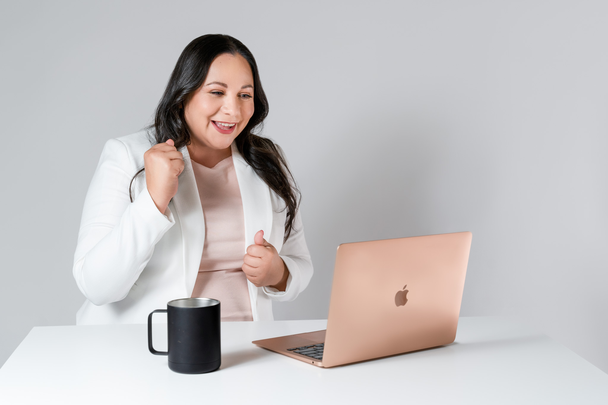 Professional woman working at desktop computer holding a mug and cheering someone on with hand raised in modern office branding session | Jessica Korff Studios Tucson, AZ