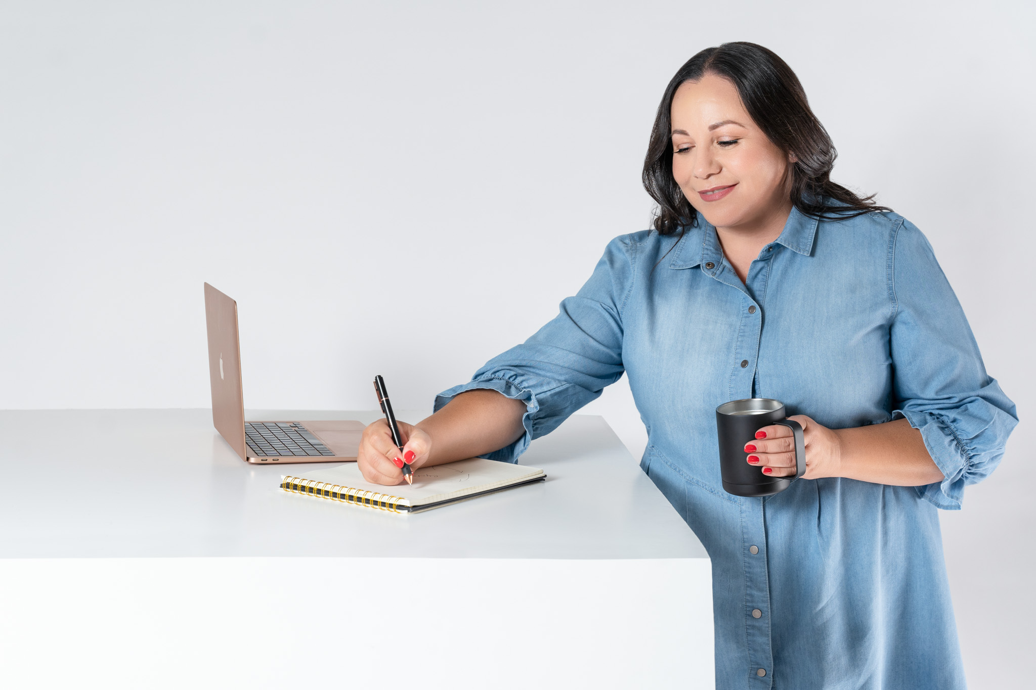 Close-up branding portrait of woman in neutral blazer, writing with a pen, holding a mug with her computer | Jessica Korff Studios Tucson, AZ