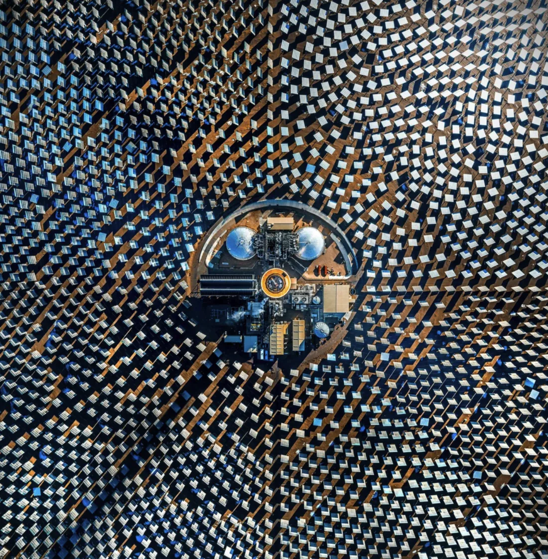 Overhead view of the solar field: more than ten thousand mirrors in concentric rings around the central tower and salt tanks.