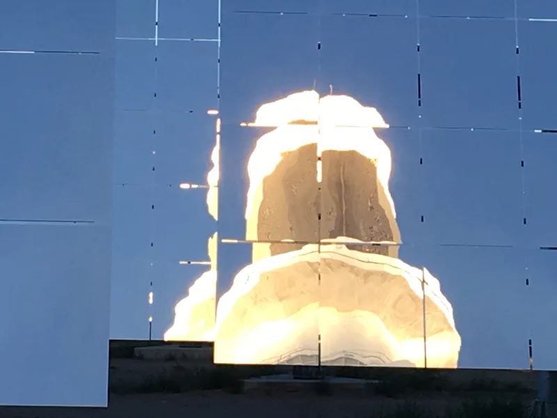 The glowing receiver seen reflected in the face of a single heliostat mirror.