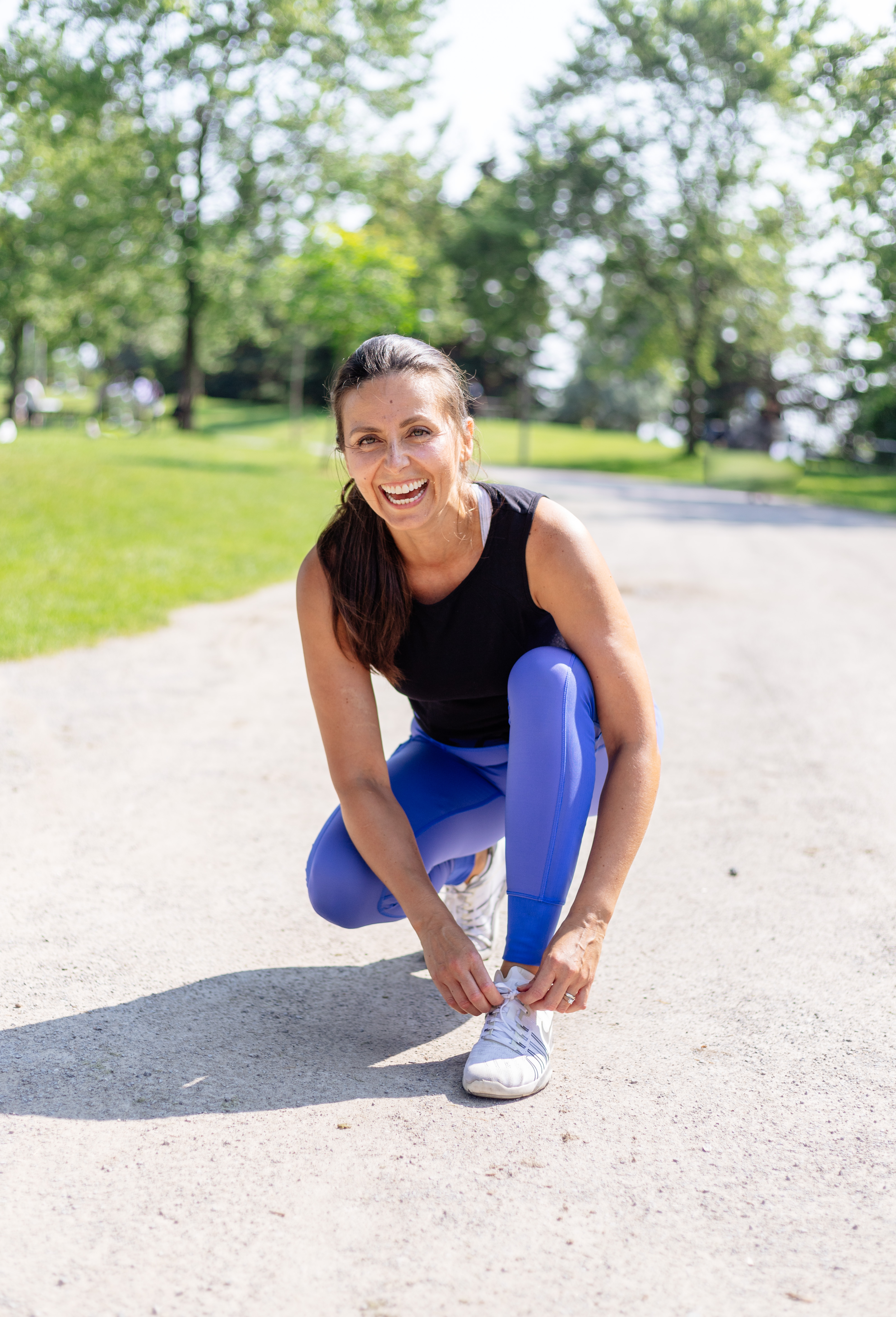 Daniela crouched tying her shoe, laughing, in the park