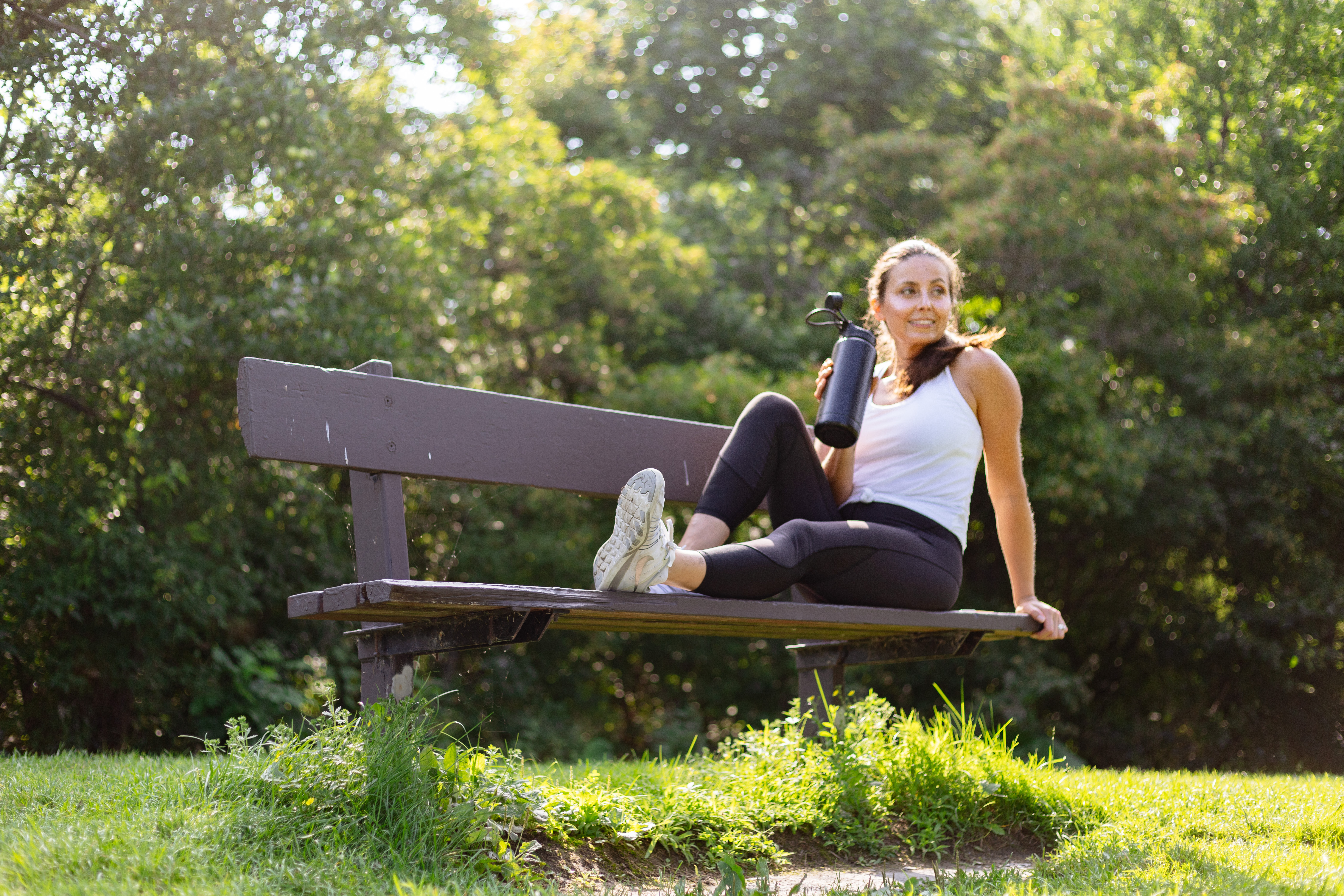 Daniela sitting on a park bench, relaxed, holding a water bottle