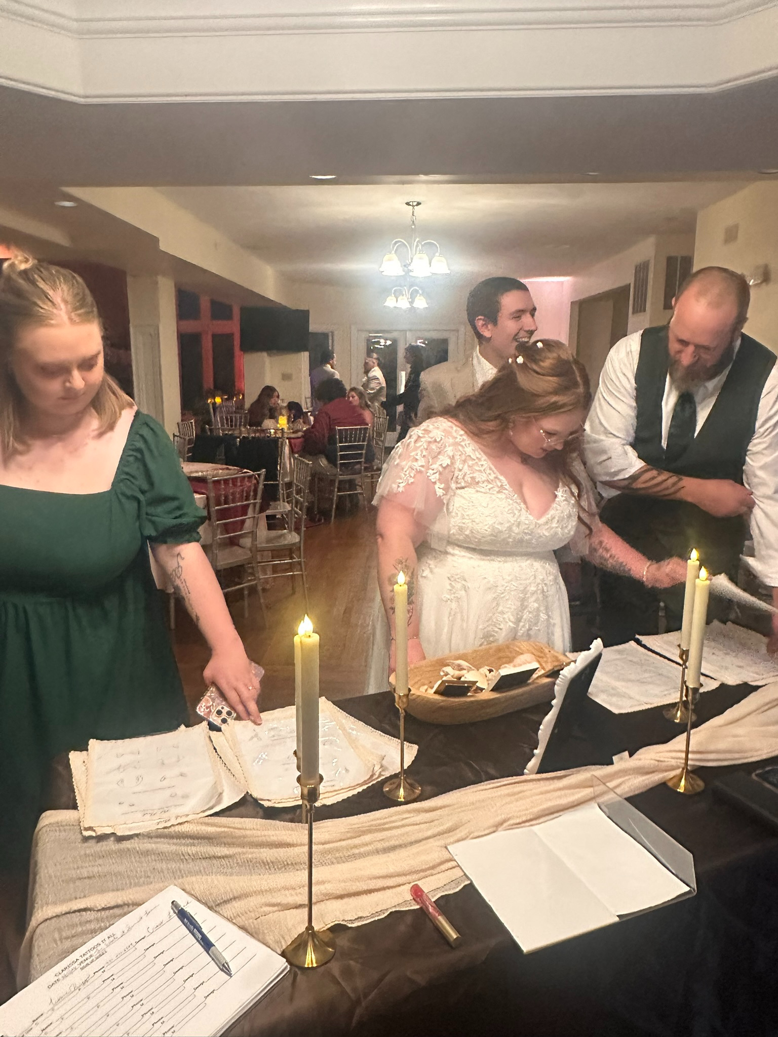Bride and wedding guests browsing Clarissa's candlelit fine line tattoo flash display at an Ohio wedding reception