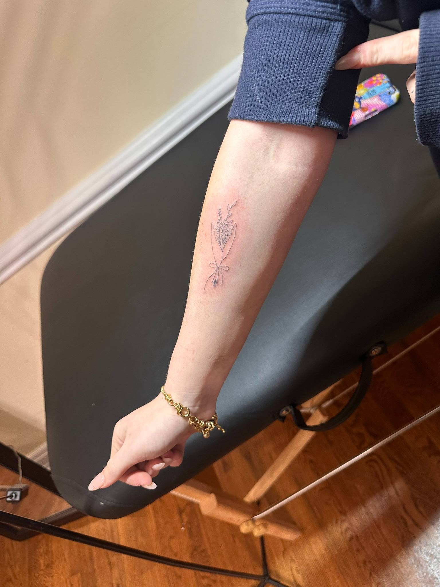 Delicate fine line floral bouquet tattoo with a ribbon on a wedding guest's forearm