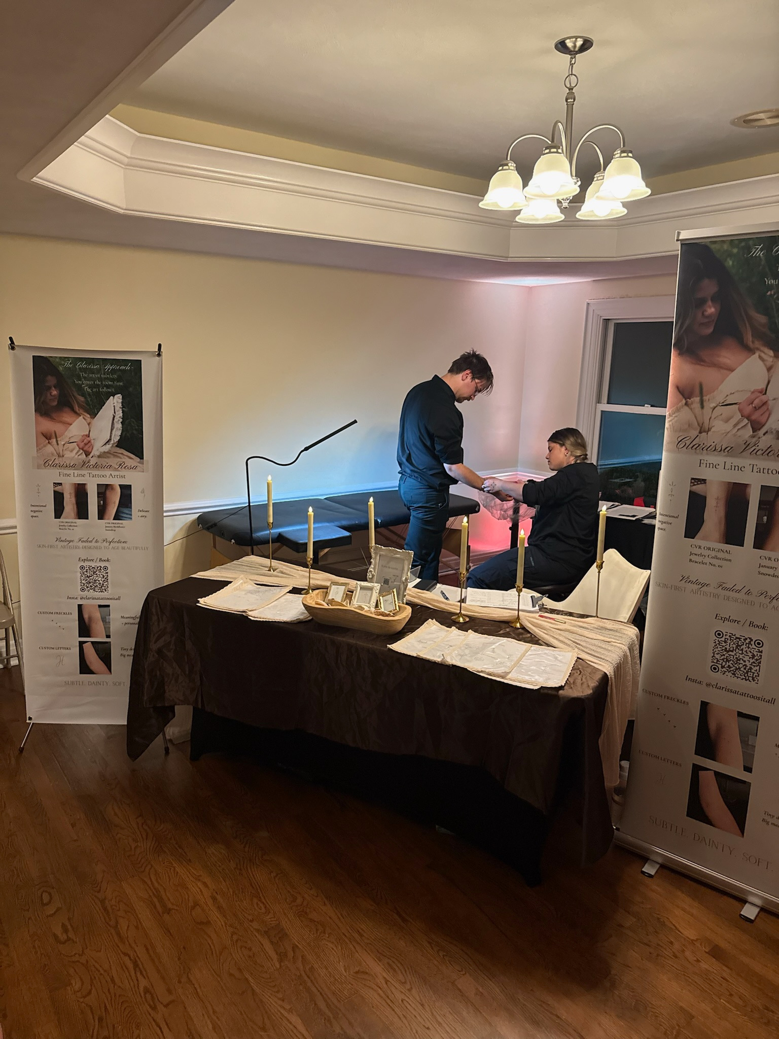 Clarissa Tattoos It All wedding tattoo booth with candlelit display table, banners and tattoo station
