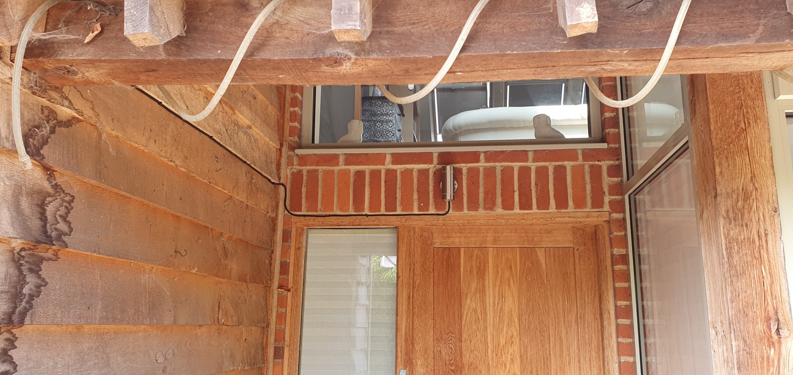 Wall light fitted between exposed oak roof trusses above a brick wall