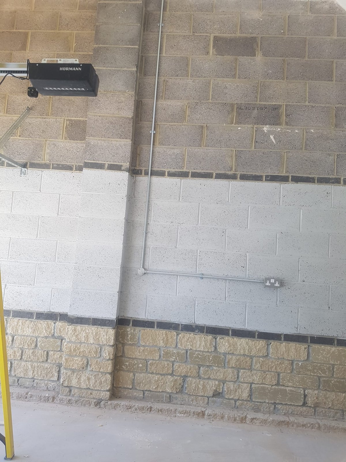 Galvanised surface conduit installed along a blockwork wall