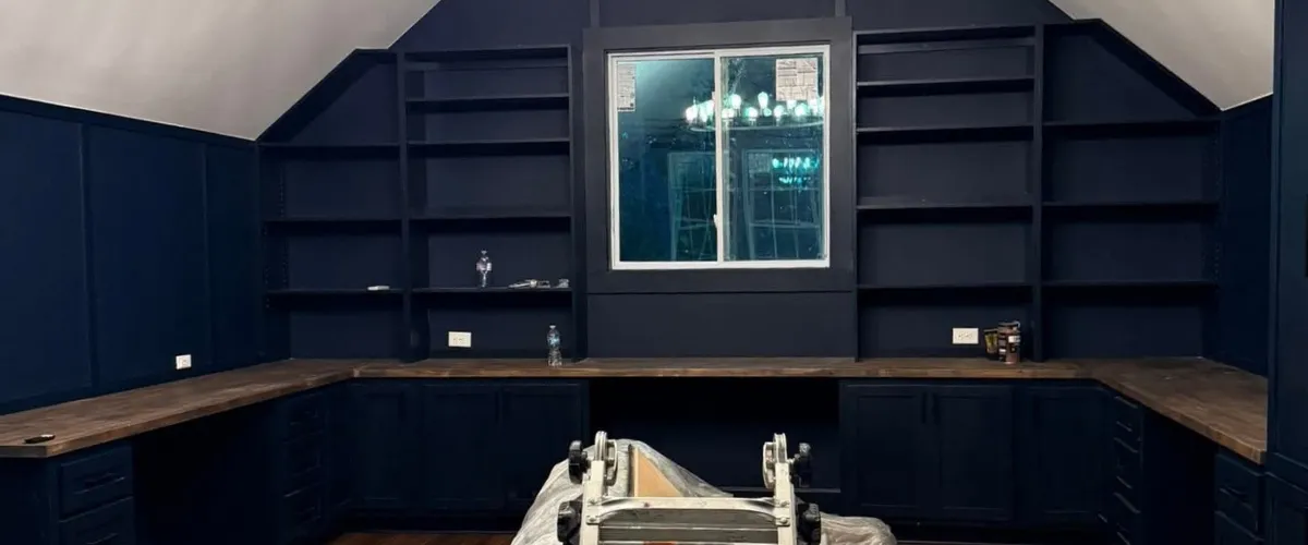 Home office setup with navy blue built-in shelves and wood countertops around a window 