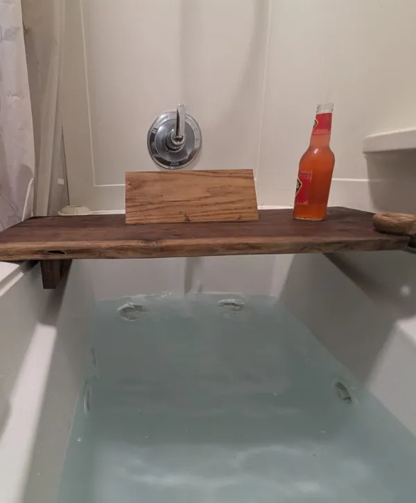 Deep bathtub filled with water and a rustic wooden tray holding a drink