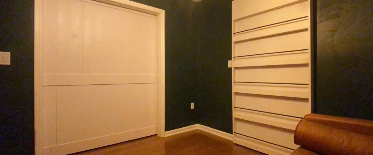 White sliding door with built-in bookshelf concealing a hidden room in a dark-painted interior