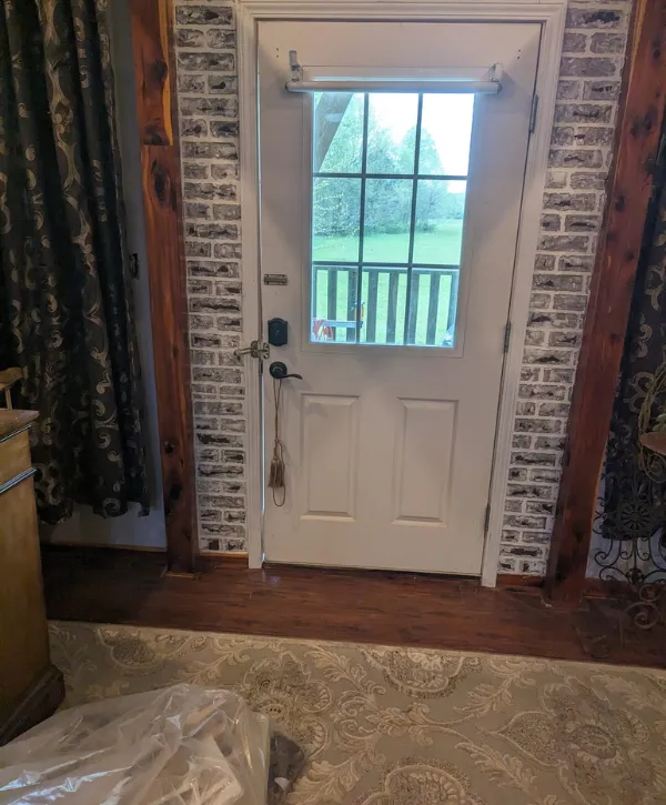 Interior white door with window panels, brick trim, and wood flooring in a rustic home