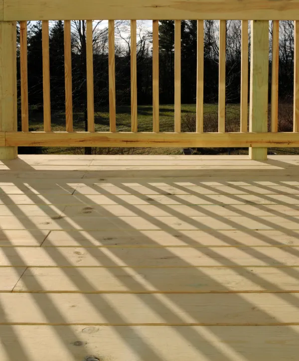 Newly built wooden deck with vertical railing casting sunlight shadows across the floor 