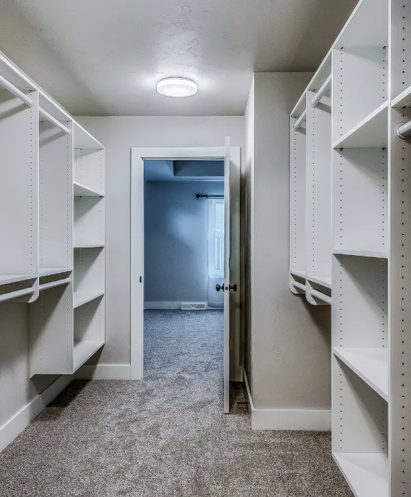 Modern white walk-in closet with carpet flooring, built-in shelving, and open doorway to adjoining room