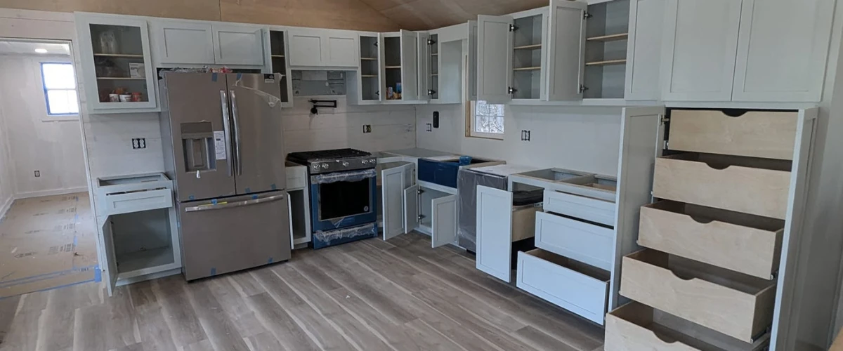 Modern kitchen remodel in progress showing light-colored cabinets, new flooring, and stainless steel appliances being installed.