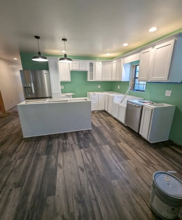 Bright kitchen renovation with white cabinets, green accent walls, and new lighting fixtures above the island.