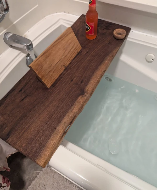 Handcrafted wooden bathtub caddy tray holding a drink bottle above a filled bathtub