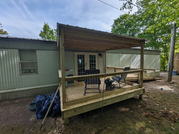 Newly built covered wooden porch attached to a mobile home with seating and tools visible.