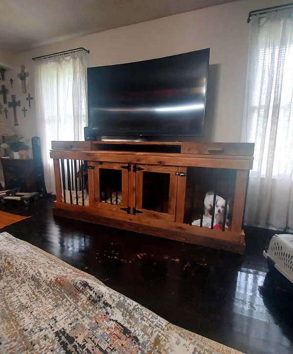 A living room featuring a curved TV on a wooden stand with built-in dog crates, one holding a small white dog.