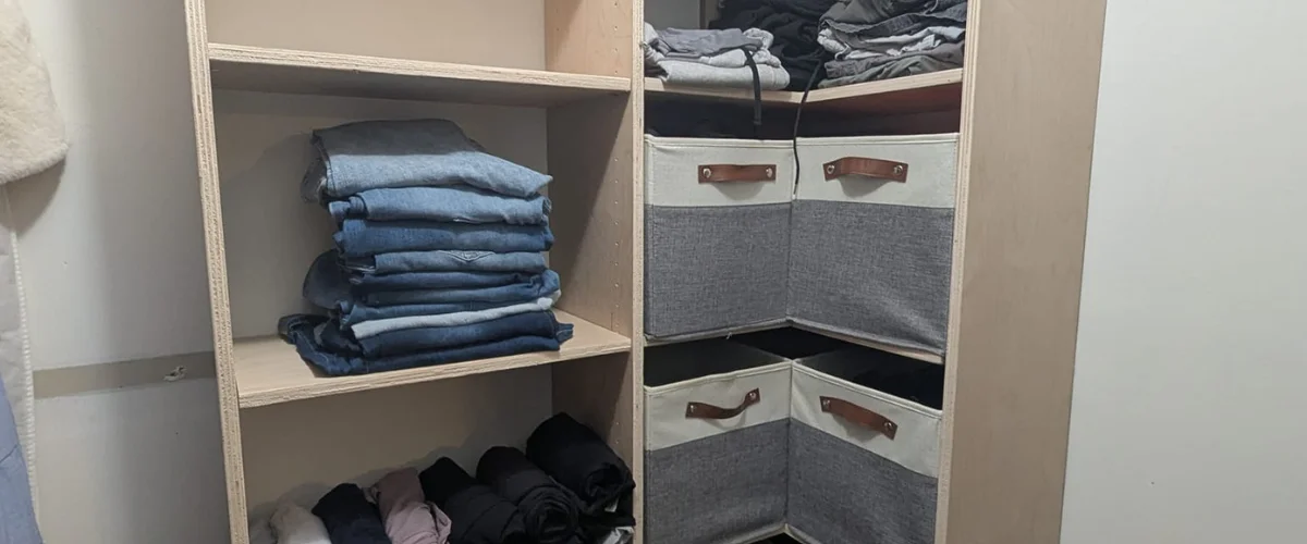 A custom wood closet with stacks of folded jeans on a shelf and gray and white fabric storage bins.