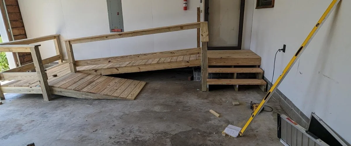 An unfinished wooden wheelchair ramp and steps leading to a door inside a garage, with a level leaning against the wall. An unfinished wooden wheelchair ramp and steps leading to a door inside a garage, with a level leaning against the wall.
