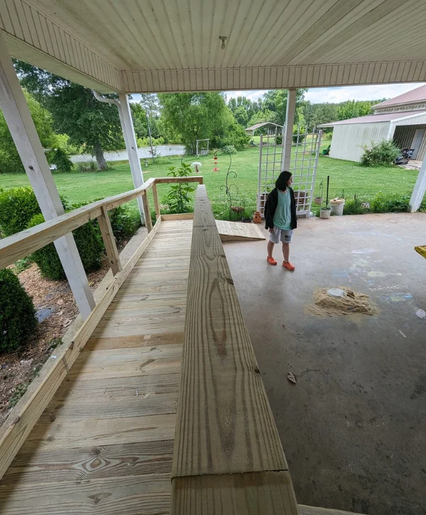 A newly constructed wooden porch ramp extending from a concrete patio, with a person standing nearby.