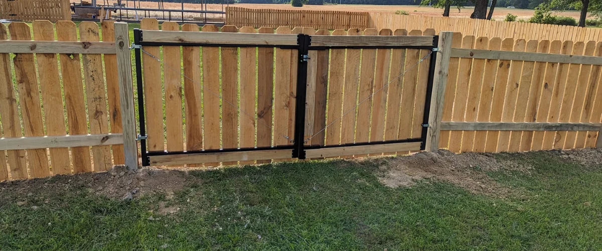 A newly installed rustic wooden privacy gate with a black metal frame, opening into a green grassy yard.