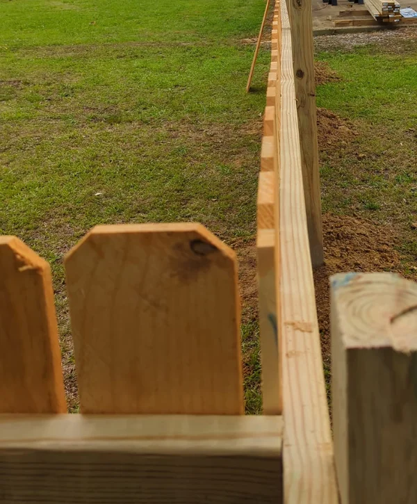 A close-up, high-angle view of newly installed wooden fence pickets and posts against green grass.